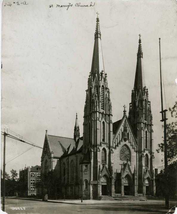 The Gothic revival church is stone-clad. The front has twin towers topped by spires on either side of the gabled entrance to the main building. There is a large circular stained-glass window above the arched front door. Long, narrow arched windows run the length of the sides.