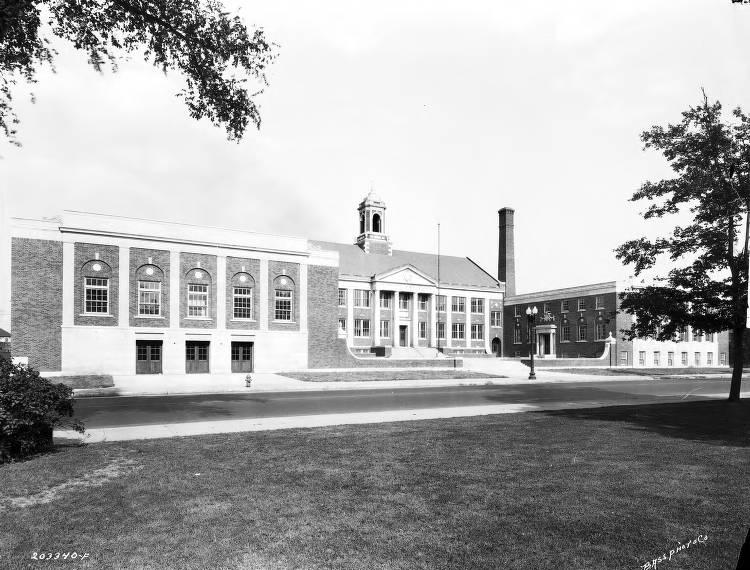 The large brick Federal style school has a central building with a large wing on each side. The central building has a cupola and a gabled entrance with columns.