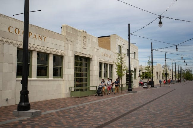 A long row of one- and two- level Art Deco buildings with limestone fronts line a broad brick boulevard.