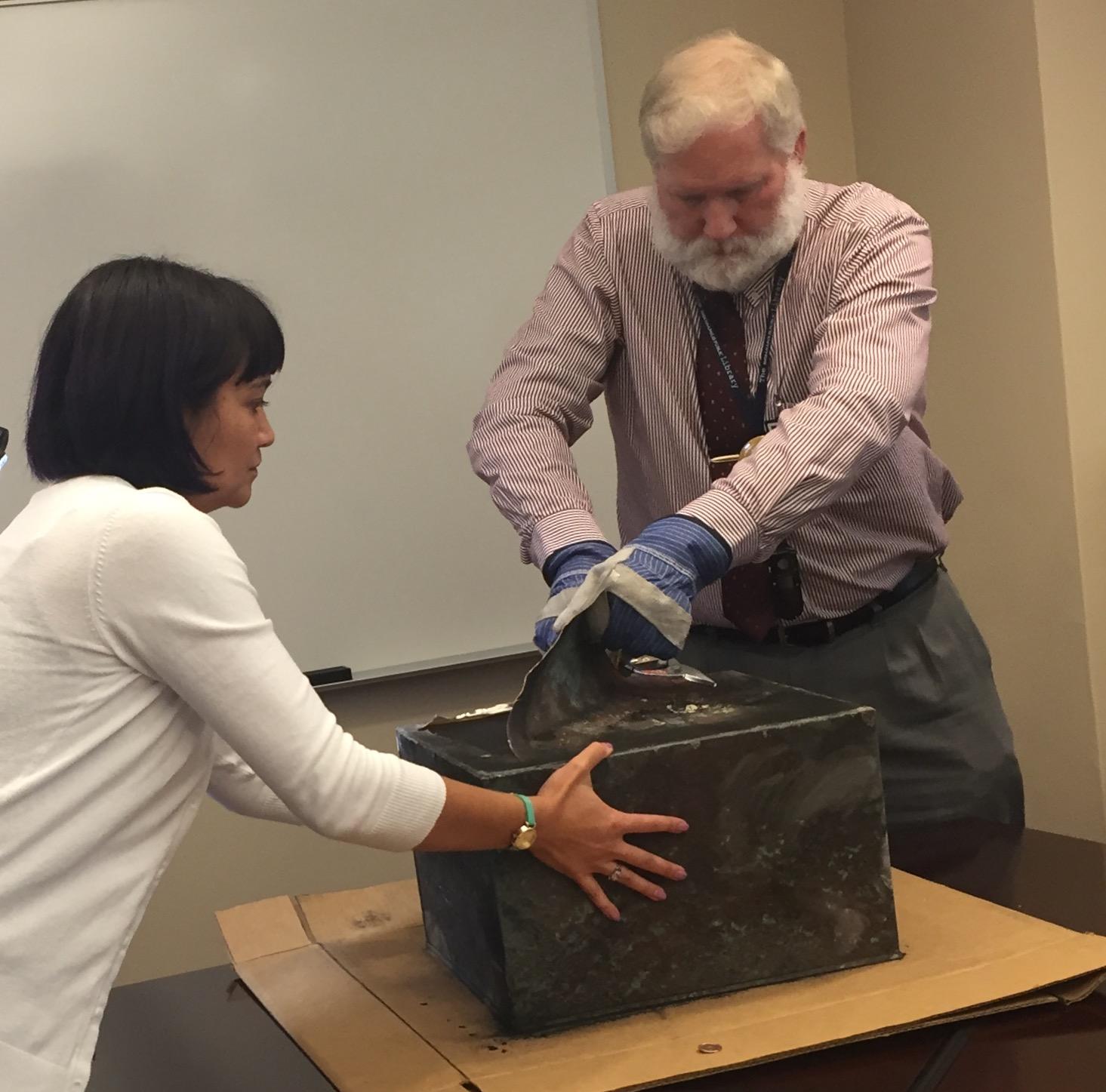 A woman holds an old box while a man opens the top of it.