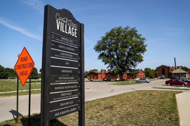 A black sign, with "Central State Village" at the top, lists the building names.