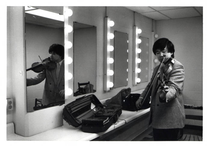 A man playing a violin stands in a dressing room.