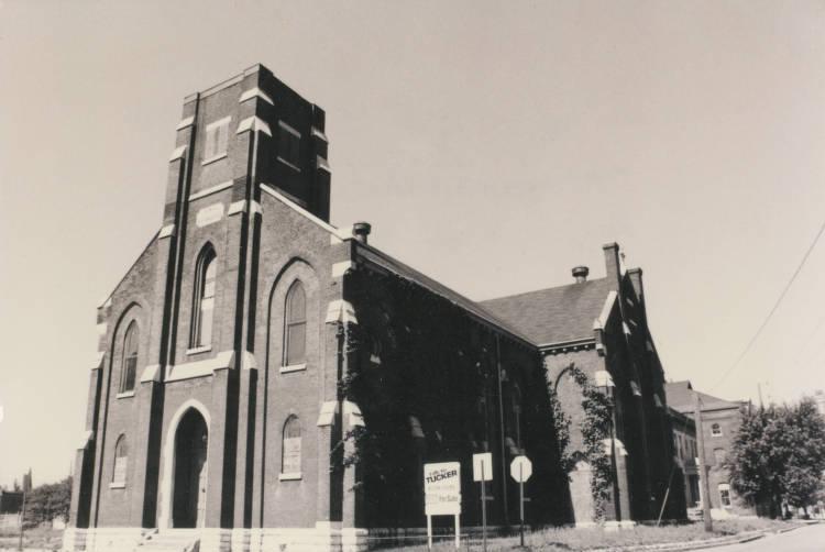 The two-story brick church has a peaked roof, arched and lancet windows and a square tower atop the front of the roof.