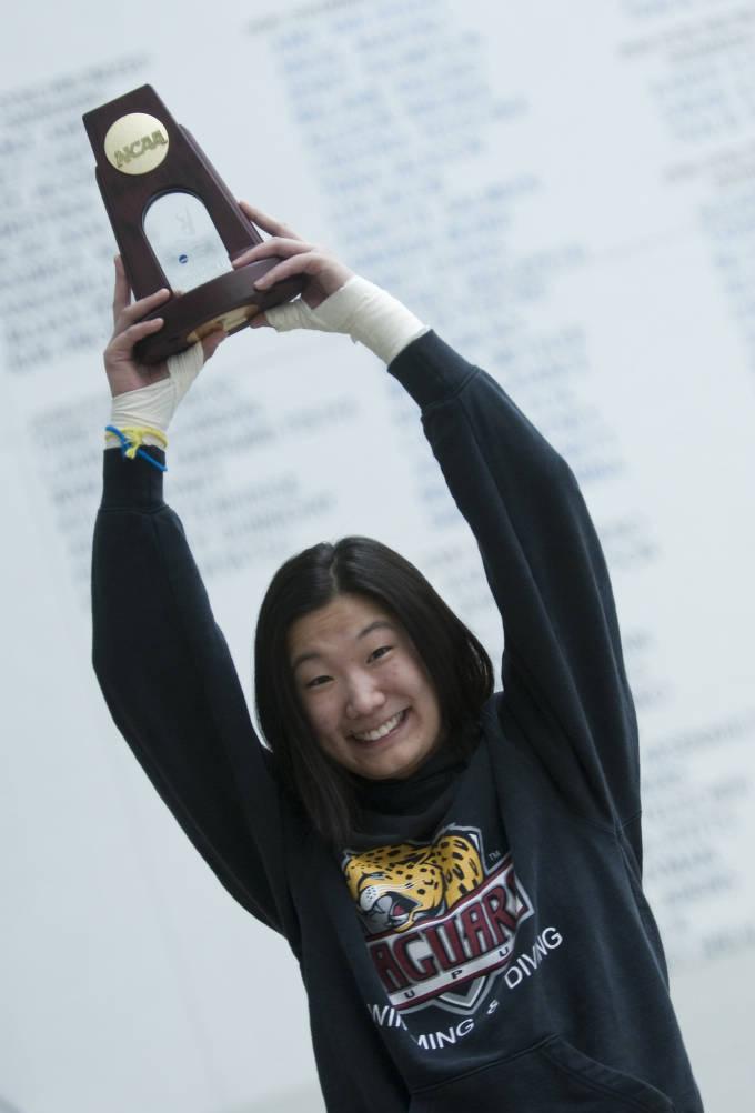 A woman holds up a trophy over her head.
