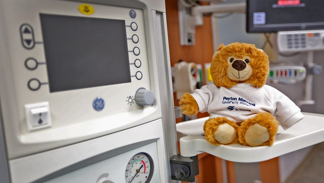 A stuffed bear sits on a table next to a medical monitor.