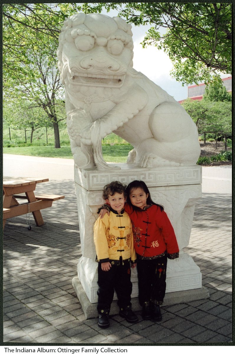 Two children pose in front of a statue of an Asian inspired dog. 