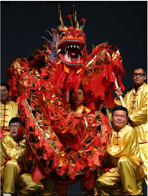 A large, bright red dragon is supported on sticks by men in yellow costumes.