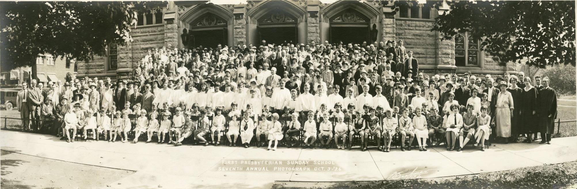 A group of people are gathered for a photograph outside of a church building. 