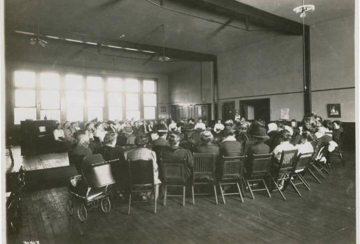 A group of women sit in chairs in a circle in a large room. 