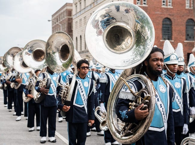 A group of tuba players line up in preparation to march in a parade.