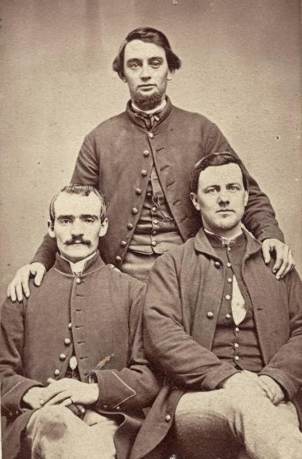 Two men are seated, while the third stands behind them.