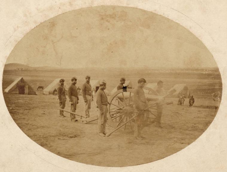 A sepia photo shows soldiers around a cannon on wheels. There are tents in the background.