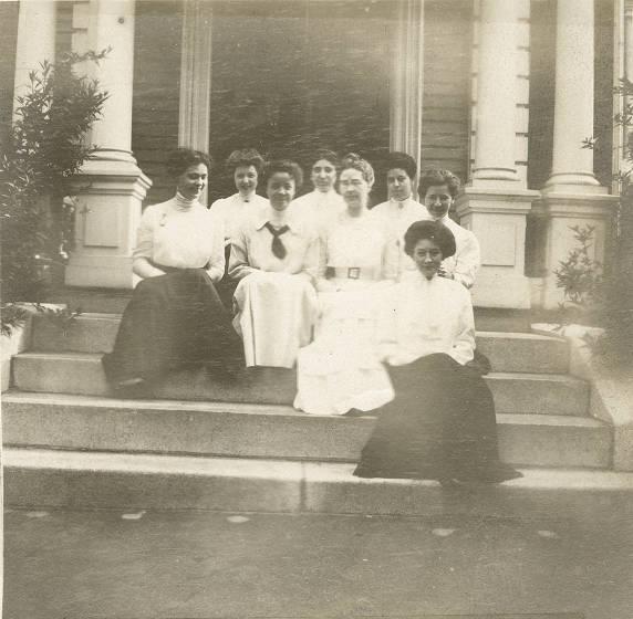 Several young women sit on the steps of a building.
