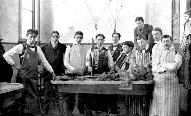 A group of men stand around a table with a cadaver on it.
