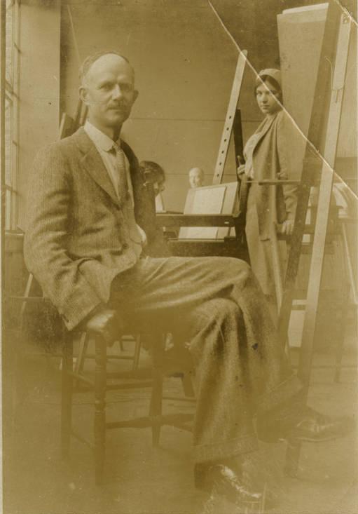 A man sits in a chair in front of an art easel. 