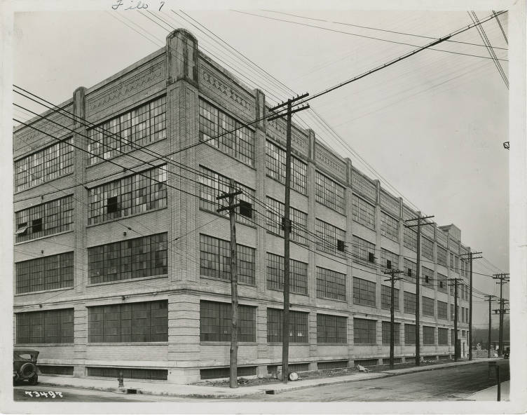 Exterior view of a four-story, L-shaped industrial building. The front facade is faced in white ceramic brick and has Art Deco style design elements.