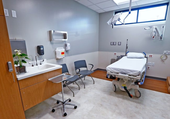 An emergency treatment room contains a hospital bed, some chairs and cabinetry with a sink.