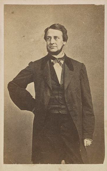A man in period clothes stands with one hand on his hip.