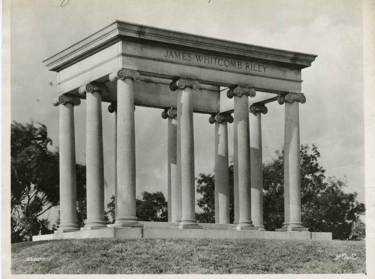 The neoclassical pavilion is composed of a concrete base with ten columns forming a rectangle. "James Whitcomb Riley" is inscribed on the top front of the monument.