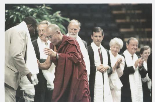 The Dalai Lama bows to a man. A row of clergy people stand in a row in the background.
