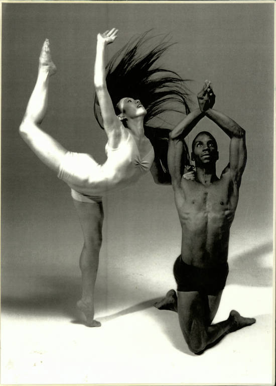 A woman doing an arabesque is next to a man in a kneeling pose.