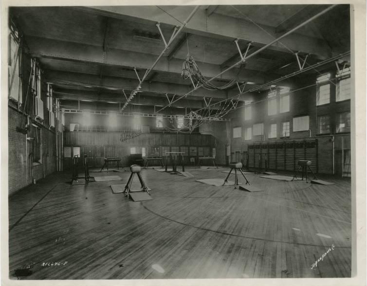 Interior view of a large open gymnasium with several pommel horses set up. 