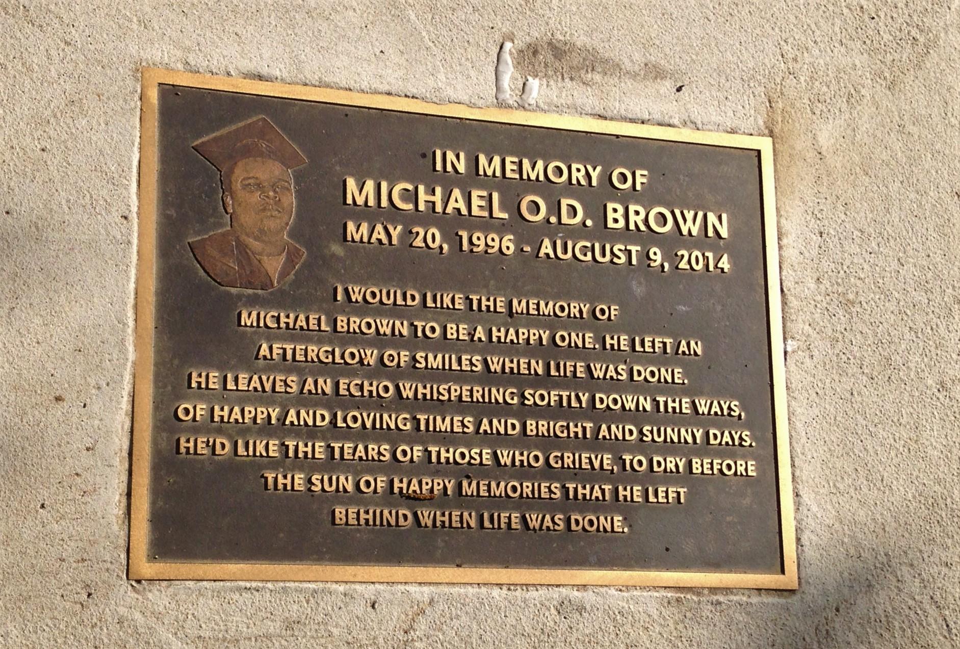 The plaque is affixed to the side of a building and includes an image of Michael Brown.