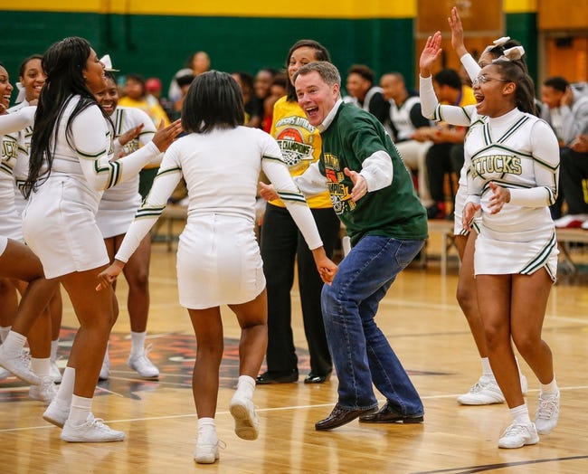 A man is surrounded by cheerleaders in the middle of a basketball court.