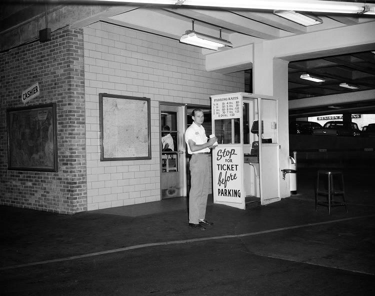 A man stands in front of a small booth which has "Stop of Ticket before Parking" on it.