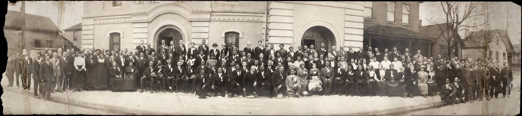 A large group of African American people stand together outside of a building.