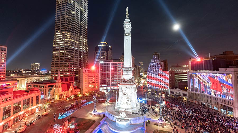 Crowds of people are gathered around the circle as the monument is illuminated and patriotic images are projected across the buildings on the circle.