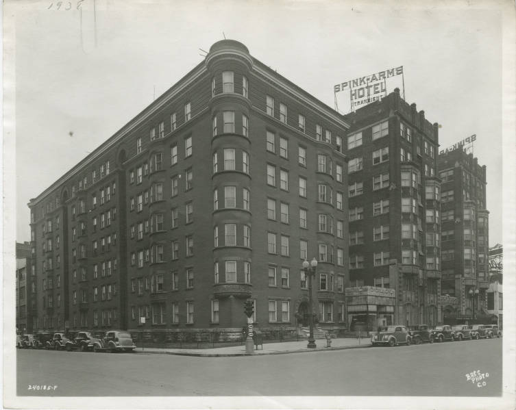 A large multi-story brick building with a sign on the roof that says "Spink-Arms Hotel."