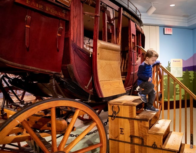 A child is exiting a stagecoach via the wooden stairs next to the coach.