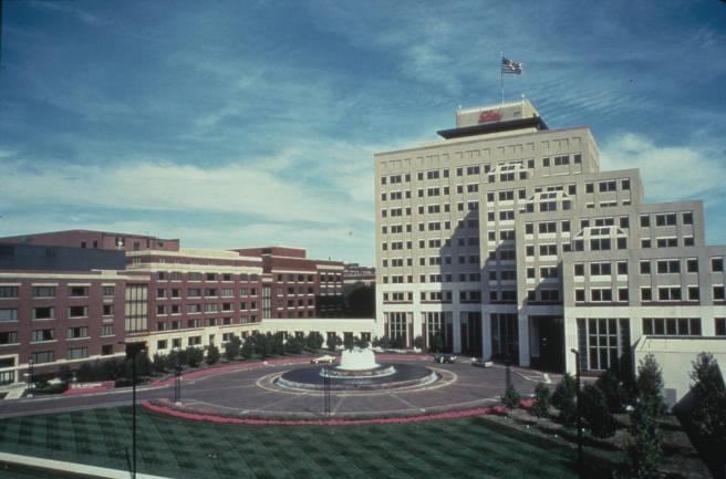 Exterior view of a large many-storied office building with a large round fountain in front of the entrance. 