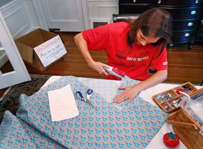 A woman works at a table which has fabric, scissors and a sewing kit on it.