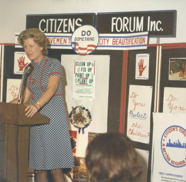 A woman speaks in front of a banner advocating for city beautification, ca. 1970