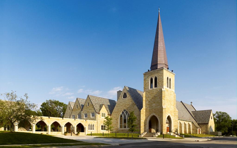 The multi-gabled, Gothic church is clad in yellow stone. There is a tower at the entrance with a 60-foot copper steeple on top.