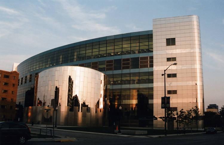 The northwestern exterior view of the Indianapolis Public Library Central Branch. The addition is a modern multi-story building with curved glass and metal front.