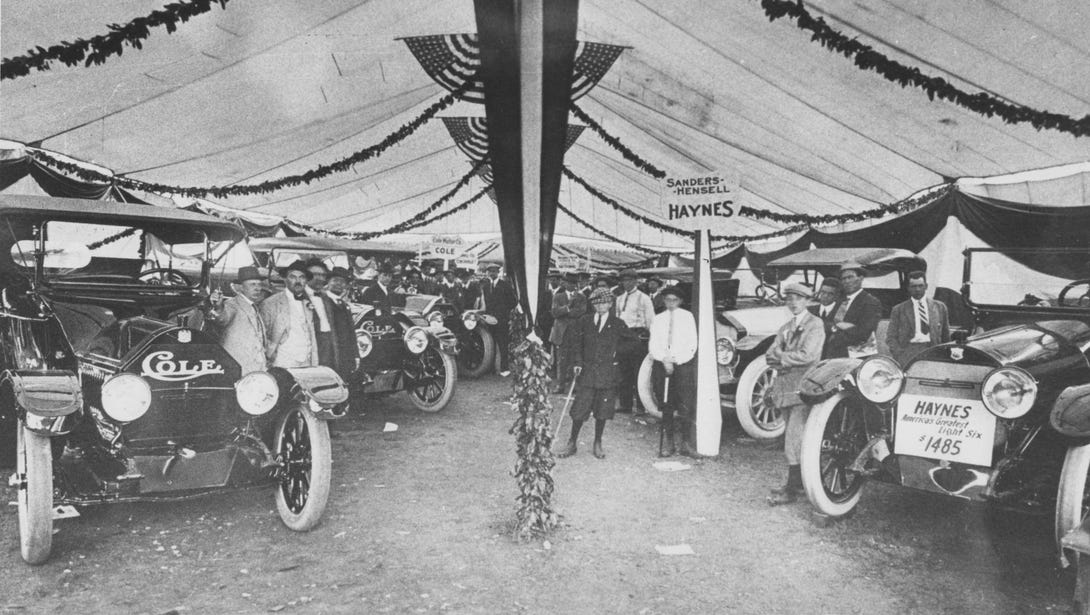 Two rows of cars and men line the inside of a large tent.
