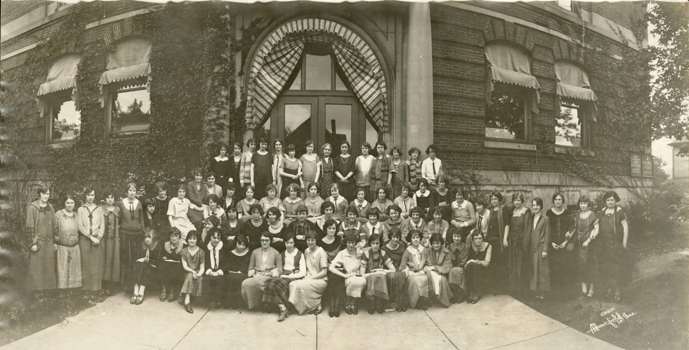 A group of young women are gathered on the steps in front of a school building. 