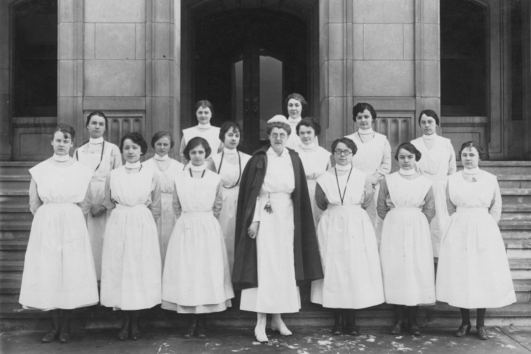 A group of women in nurse uniforms pose on steps in front of a building.