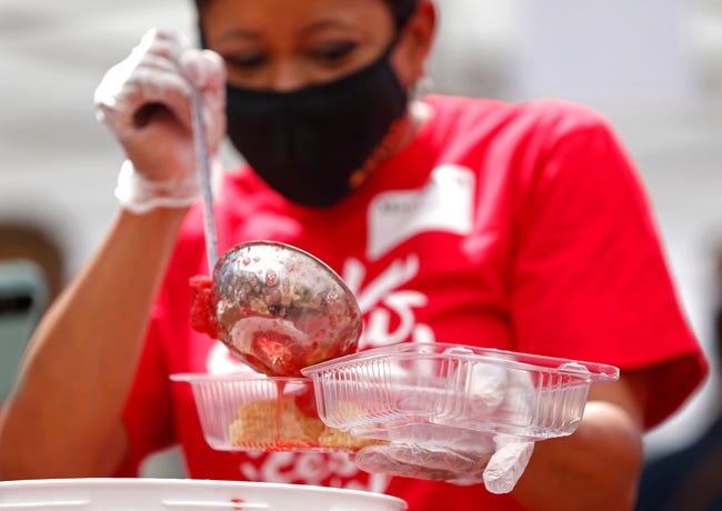 A woman wearing a Covid mask ladles strawberries into a clear, plastic container.