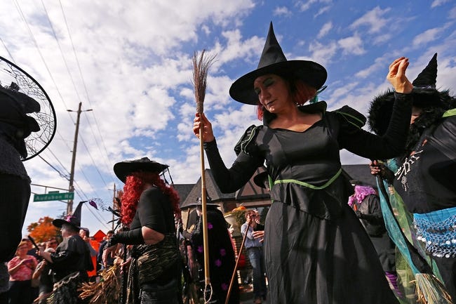 People in black outfits and pointy hats gather in a street.