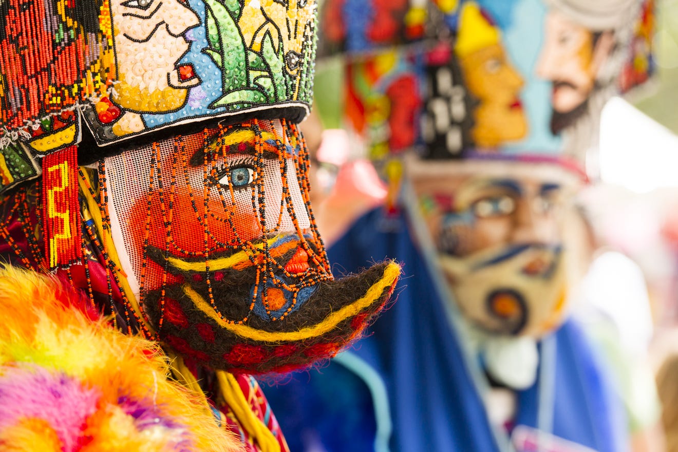 The performer wears an elaborate and colorfully painted and beaded head covering and outfit.