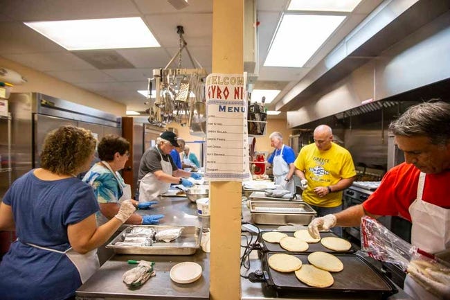People work at two long, facing rows of food stations in an industrial kitchen.