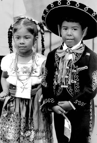A boy is wearing a Mariachi outfit and standing beside a girl who is wearing an embroidered blouse and skirt.