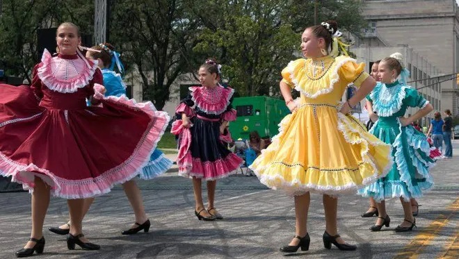 Girls in brightly-colored dresses perform in the street.