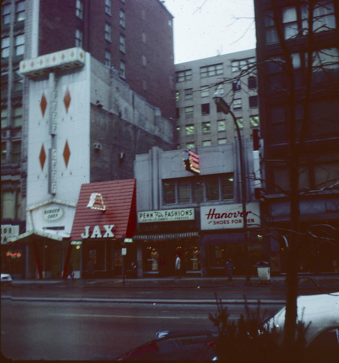 A tall, narrow building decorated with four diamond shapes on the facade stands between traditional-looking buildings. The roof eave is banded by two rows of diamond shapes.