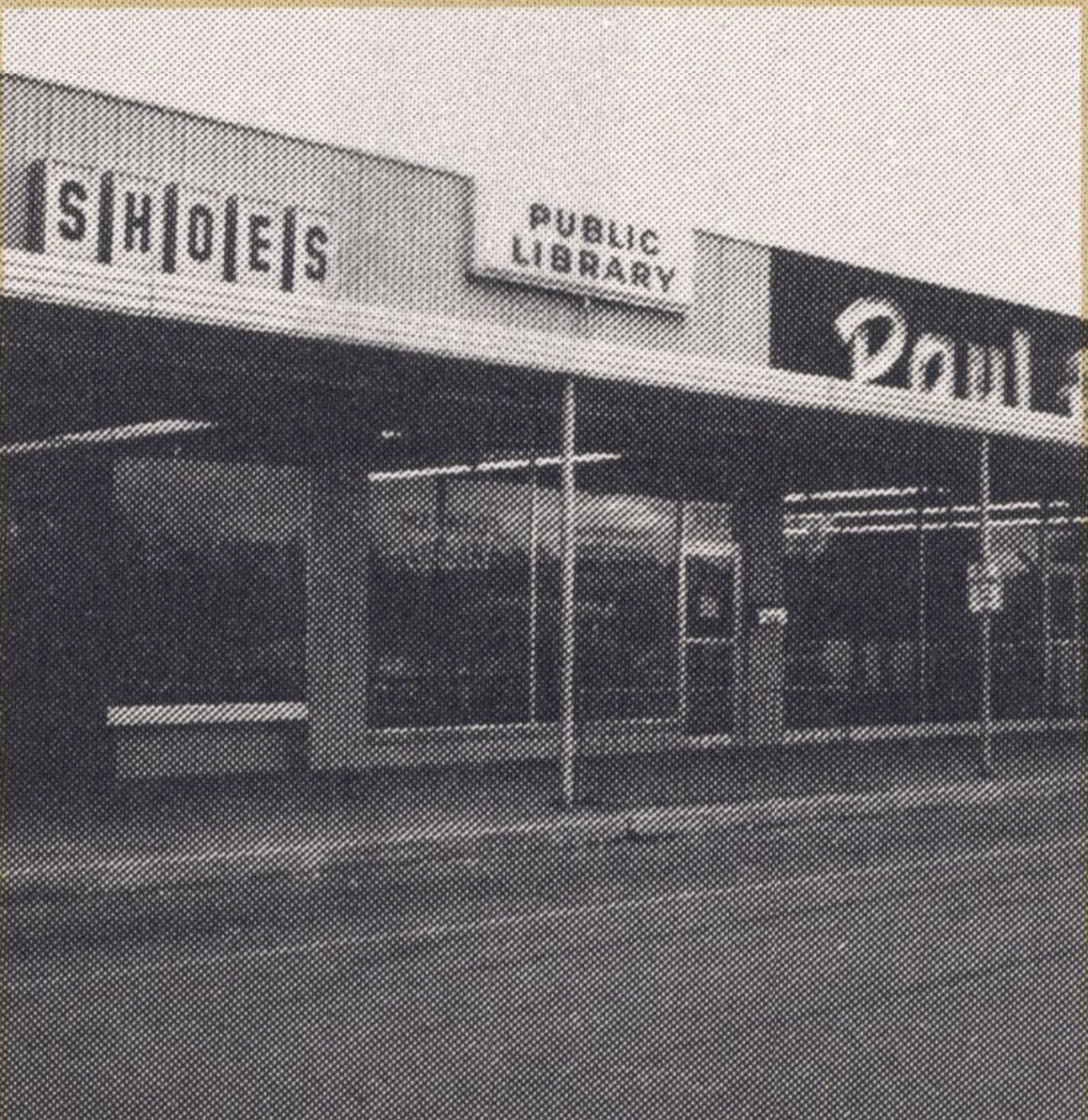 View of a shopping center store front. Signs on the top of the center read Shoes, Public Library, and Paul.