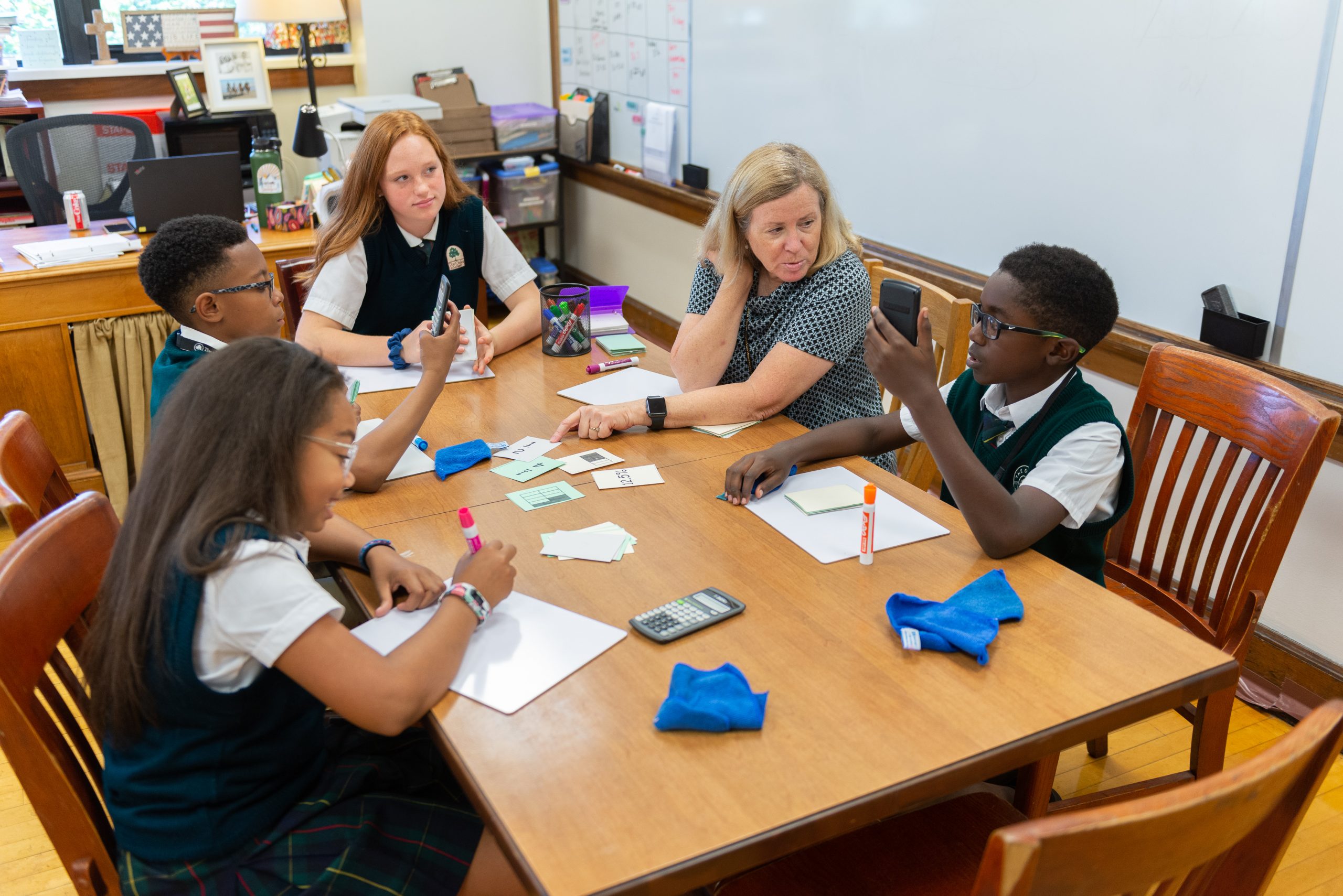 Four students sit around a table with a teacher. 